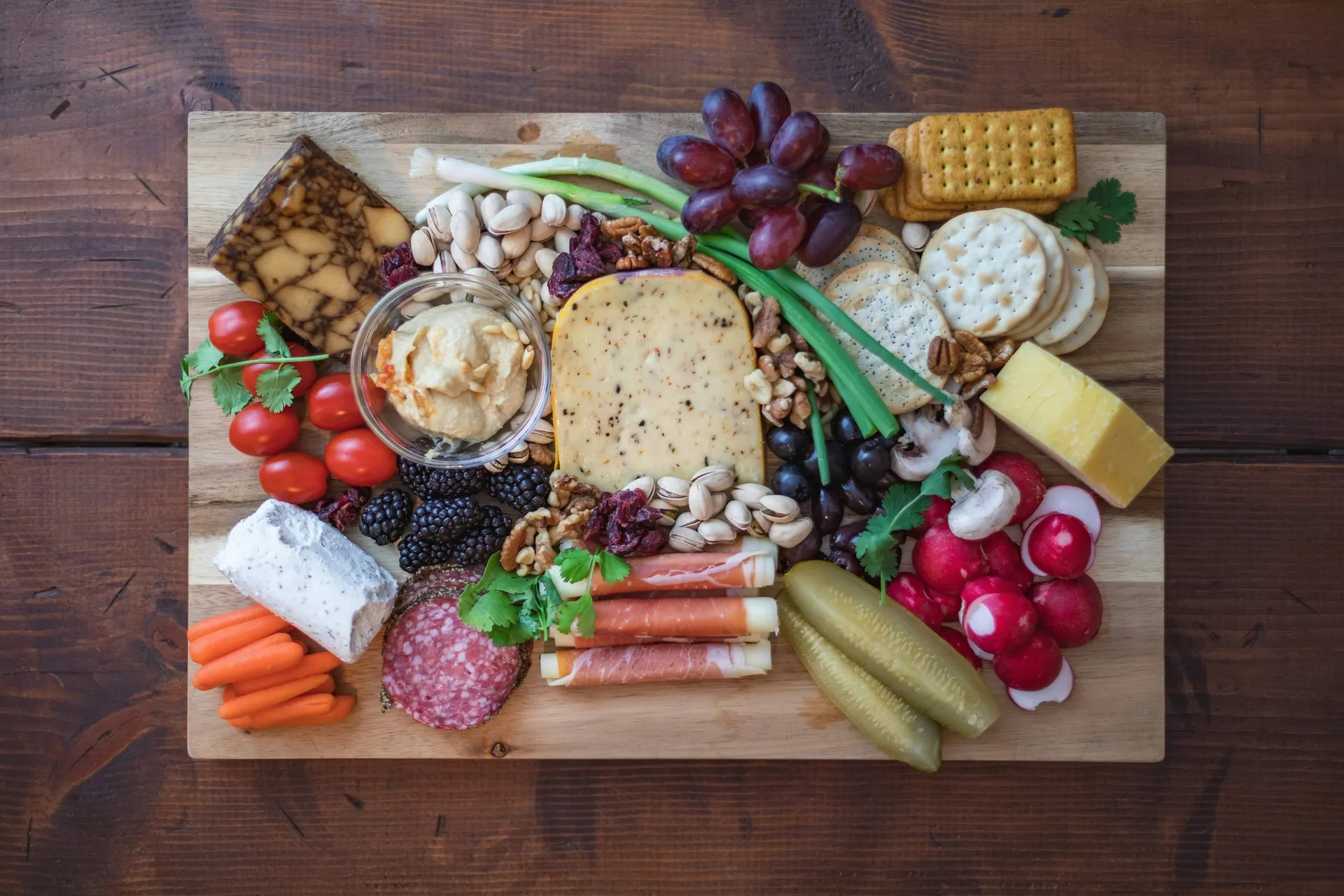 Rijk gevulde borrelplank met kazen, salami, rauwe ham, crackers, druiven en radijsjes op donker hout